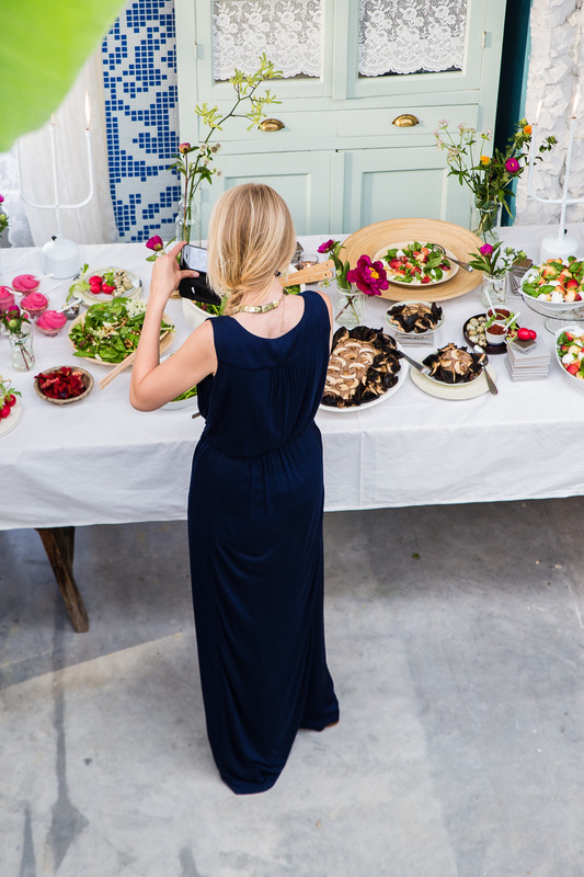 een feestelijke tafel met heerlijke homemade gerechten op prachtig serviesgoed, veldbloemen in vaasjes en een gast die hier met haar smartphone een foto van maakt. 