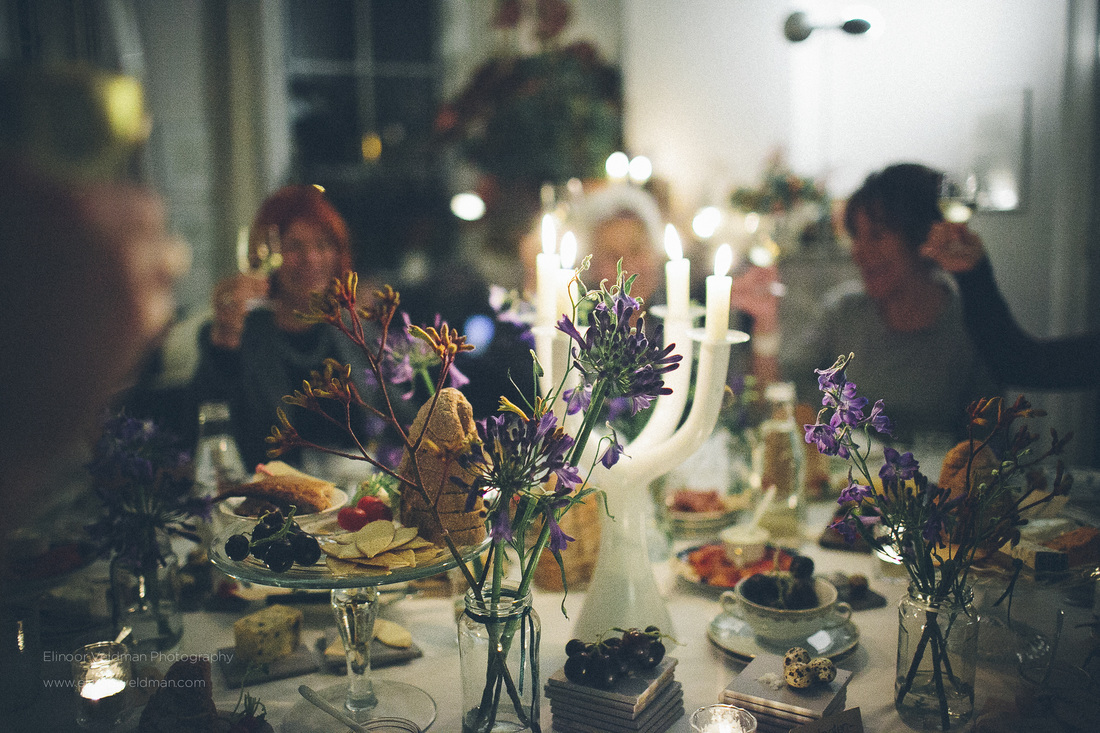 sfeerbeeld van eetlandschap op tafel met veldbloemen, kaarsen, heerlijke gerechten en blije proostende mensen